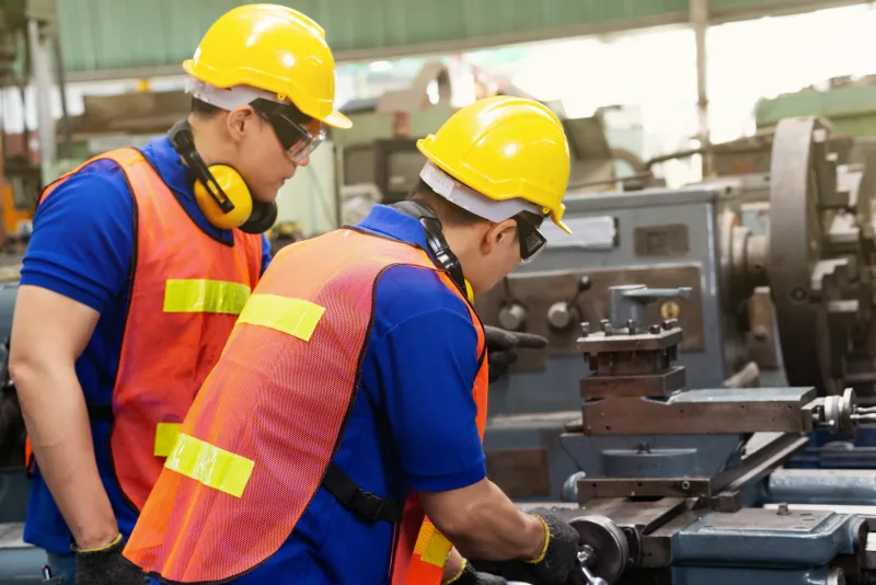 Two machinists in hard hats and safety vests on a shop floor