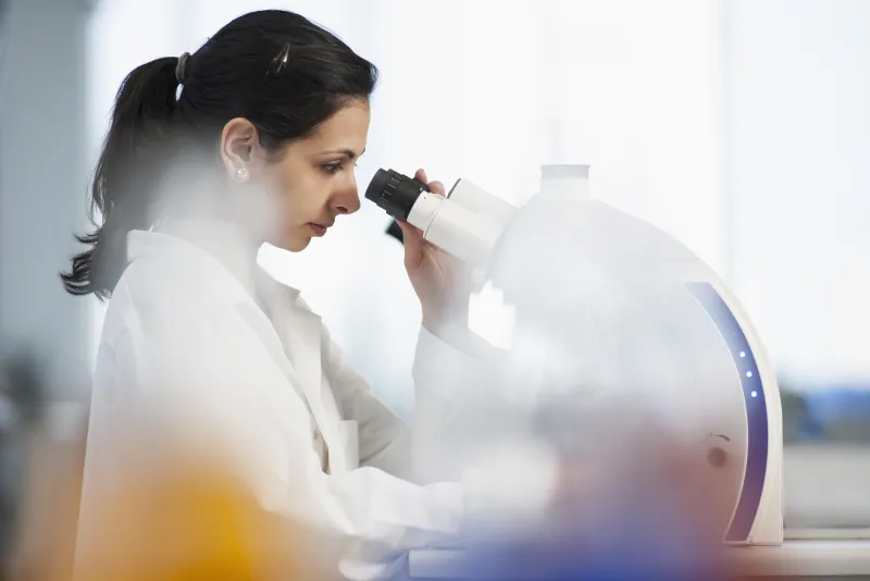 A lab technician looking through a microscope
